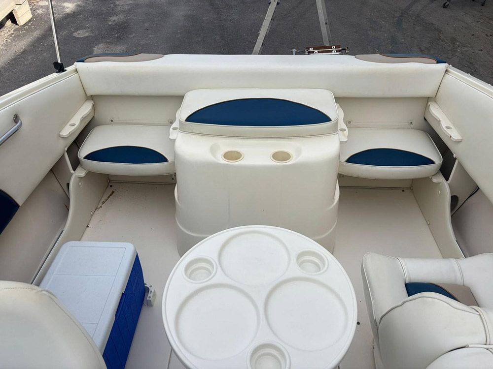 Zona de estar en el barco con bancos blancos, cojines azules y una mesa redonda blanca en la cubierta.