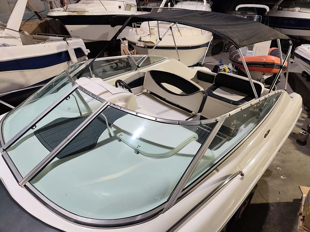 Una lancha rápida blanca con parabrisas y asientos azules atracada entre otras embarcaciones en un puerto deportivo.