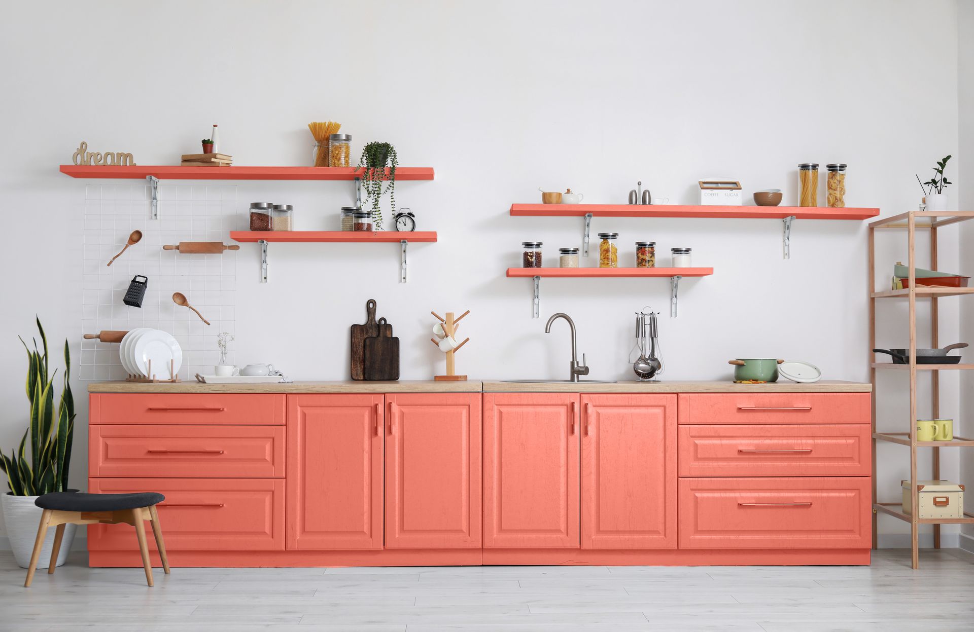 Cuisine corail avec murs blancs, étagères ouvertes, plantes en pot et tabouret en bois près du comptoir.
