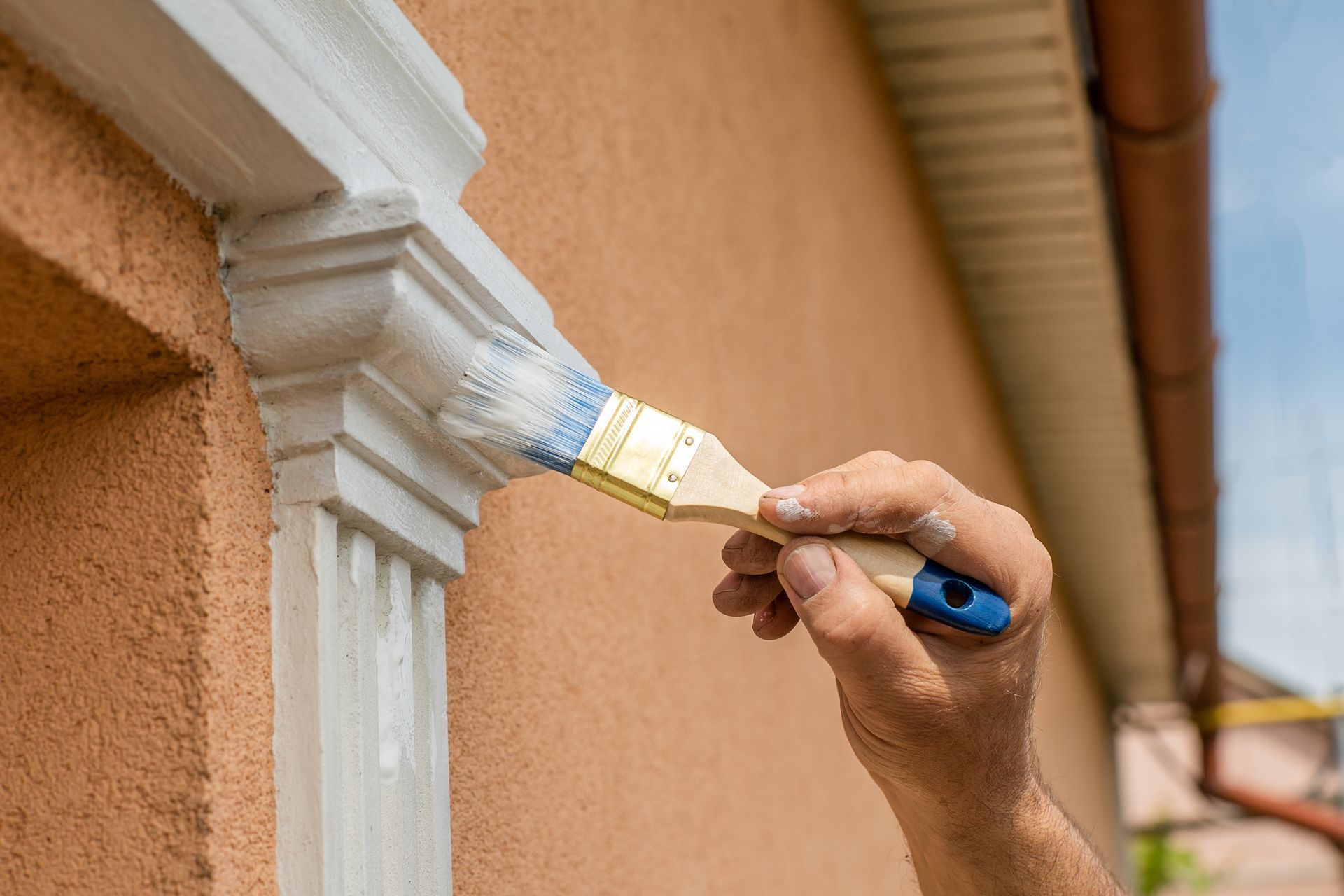 Une main peint au pinceau une bordure blanche sur un mur extérieur orange.
