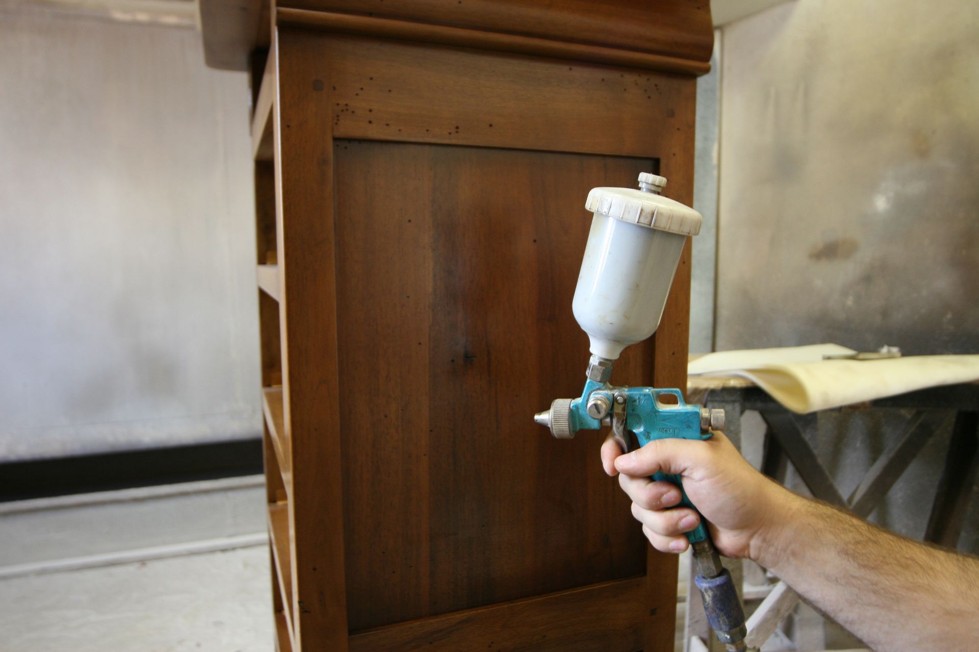 Application manuelle d'une finition au pistolet à peinture sur un meuble en bois dans un atelier