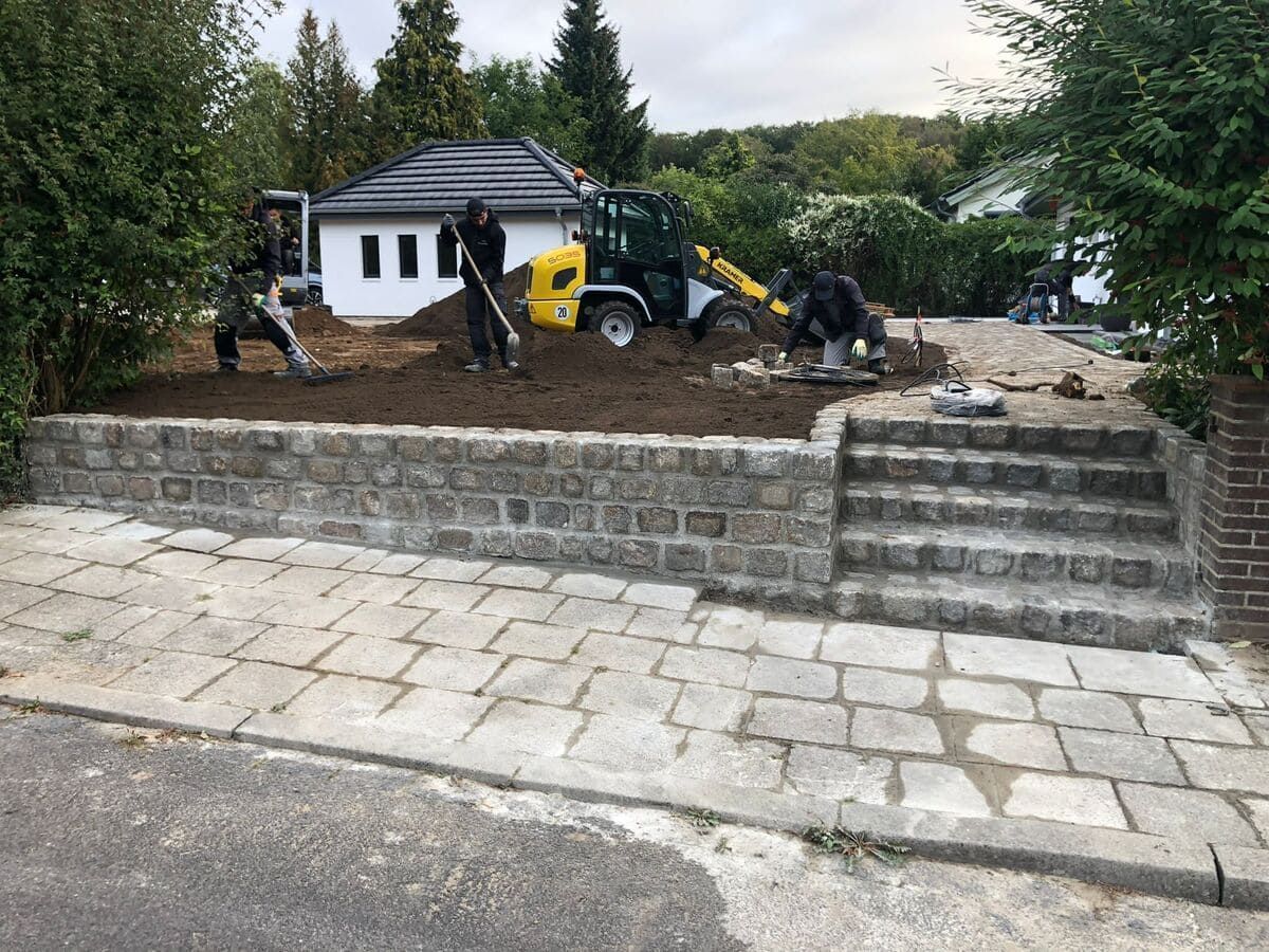 Eine Gruppe von Menschen arbeitet an einer Einfahrt vor einem Haus.