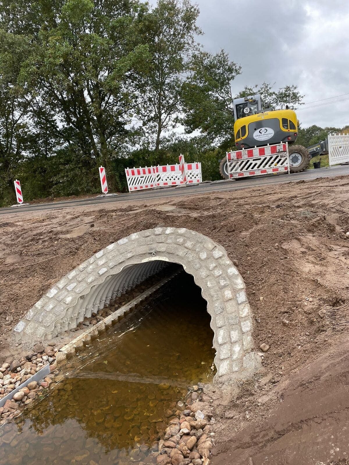 Ein gelber Bagger fährt eine Straße entlang neben einem Betontunnel.