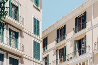 Edificios de color beige con persianas verdes y pequeños balcones contra un cielo azul.