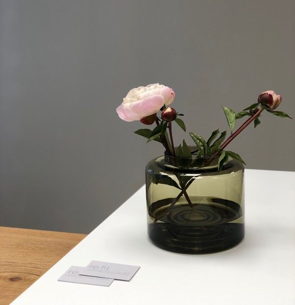 Zarte rosa Pfingstrose mit Knospen in rundem, transparentem grauem Glasvase auf weißem Tisch