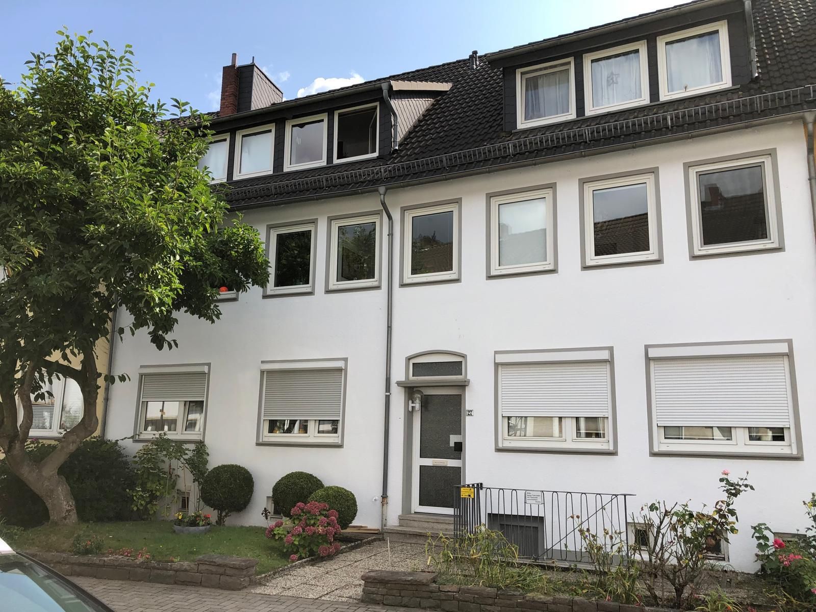 Weißes, mehrstöckiges Gebäude mit vielen Fenstern; davor Baum und Sträucher.