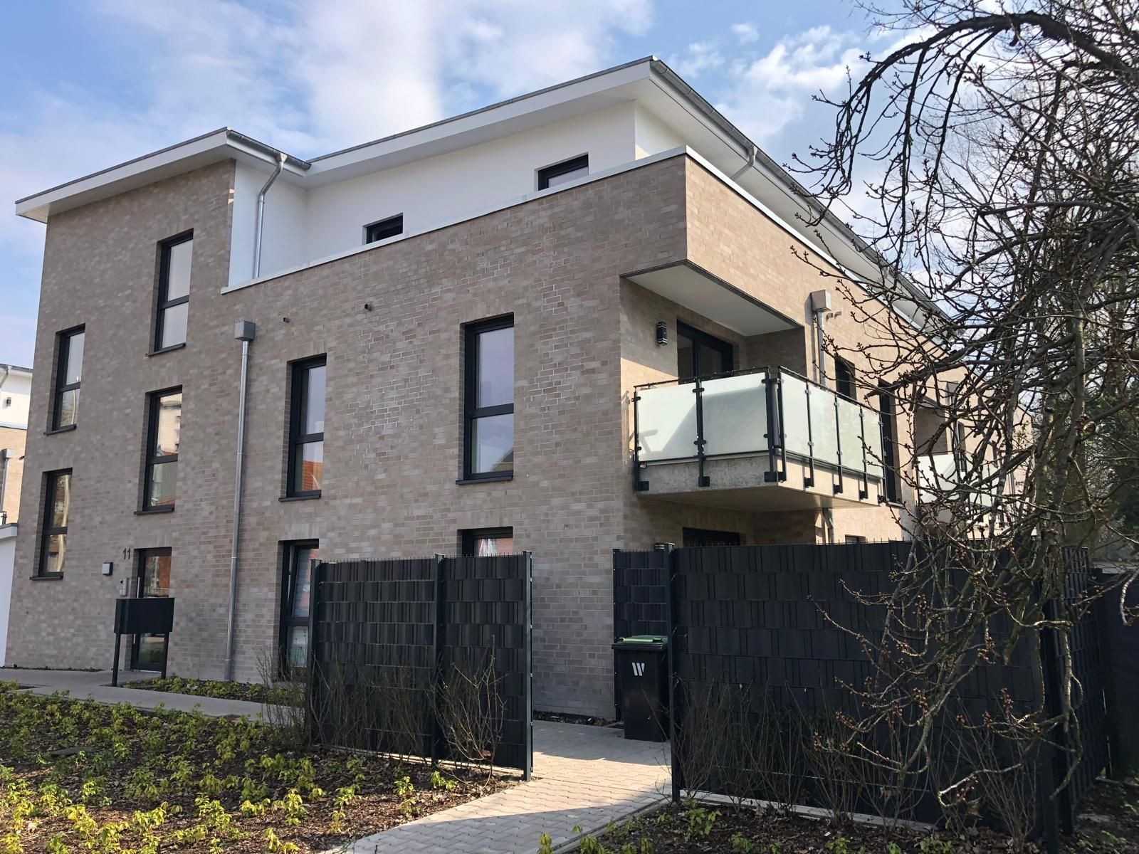 Mehrstöckiges Backsteingebäude mit schwarz umrandeten Fenstern, Balkon und dunklem Zaun.
