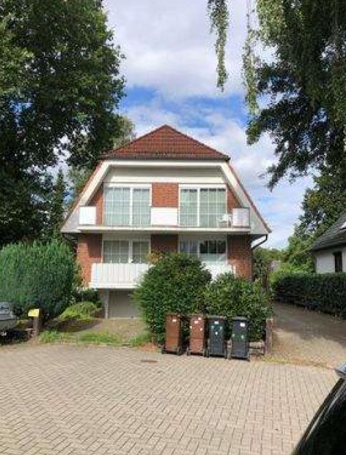 Backsteinhaus mit rotem Dach, weißen Balkonen und Gartenanlage, davor geparkte Mülltonnen.