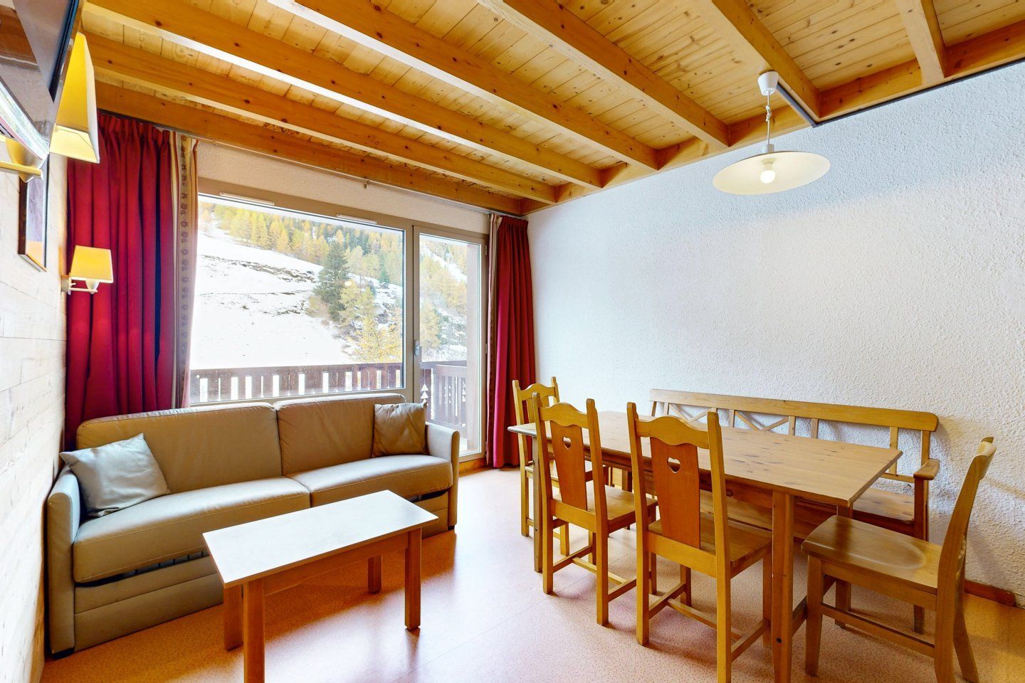 Living room with wooden ceiling, a sofa, dining table, and a balcony view of snowy mountains.