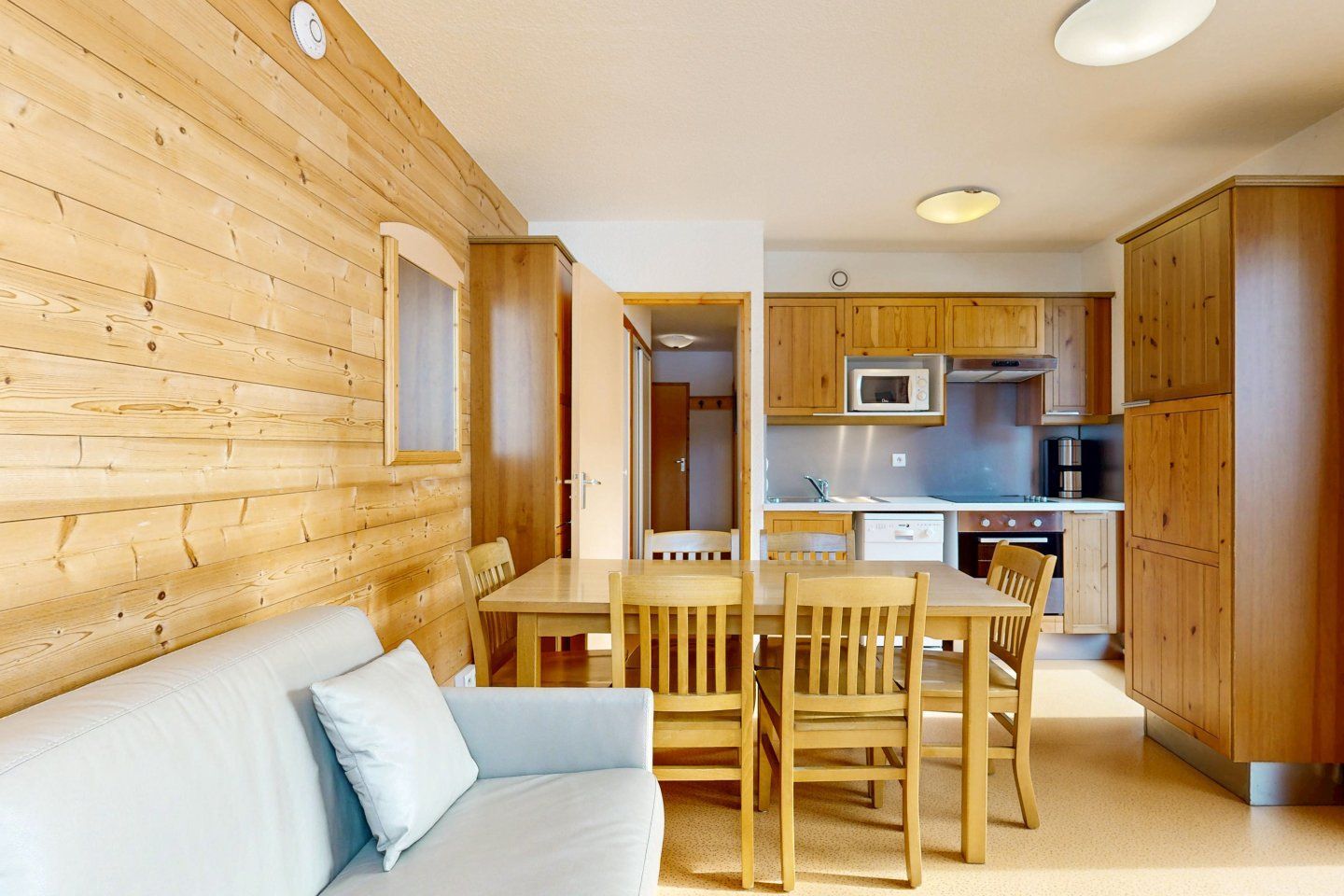 Cozy wooden-paneled room with a dining area, kitchen, and light blue sofa.