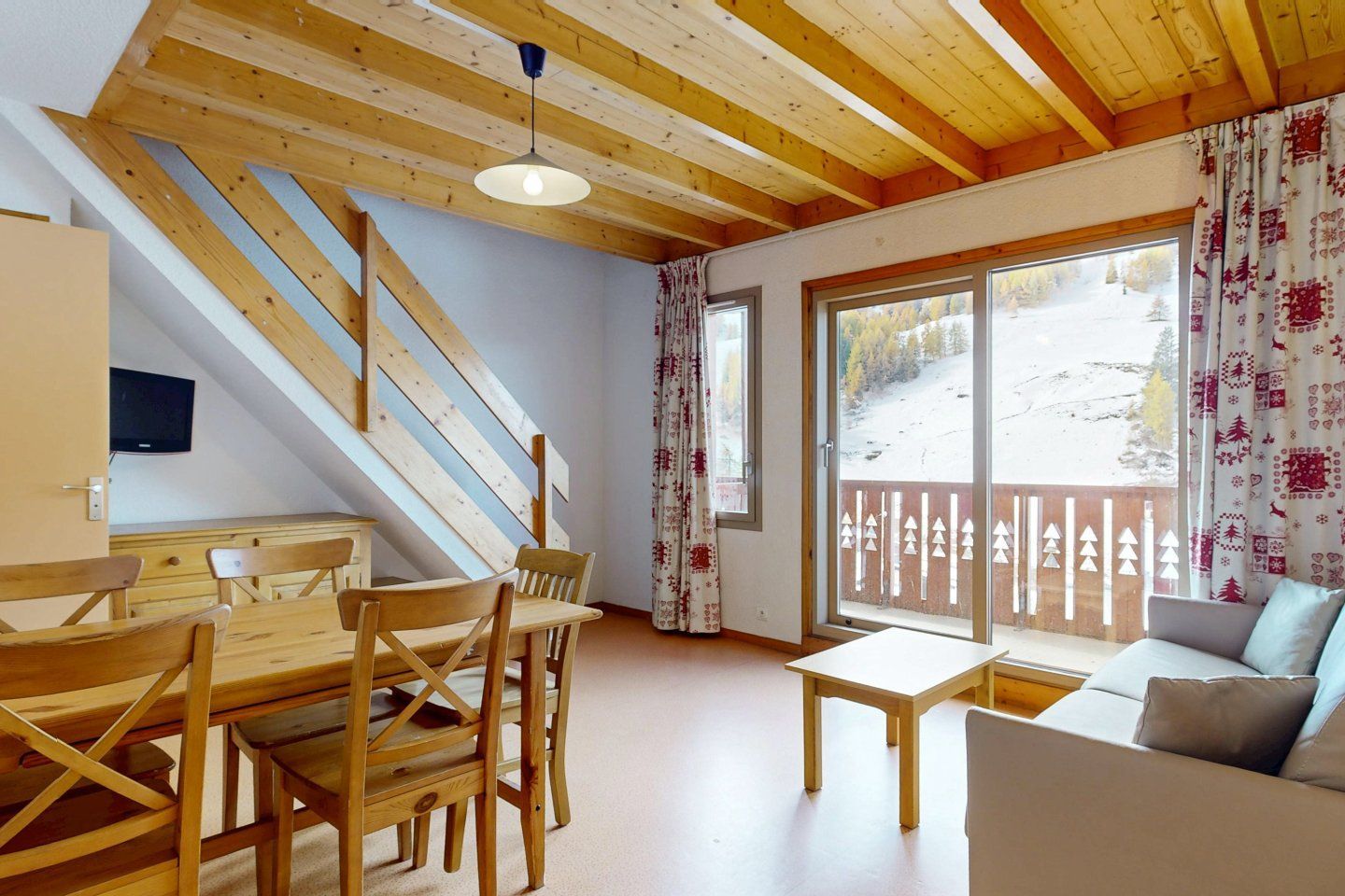 Cozy living area with wooden beams and dining table, balcony with mountain view.