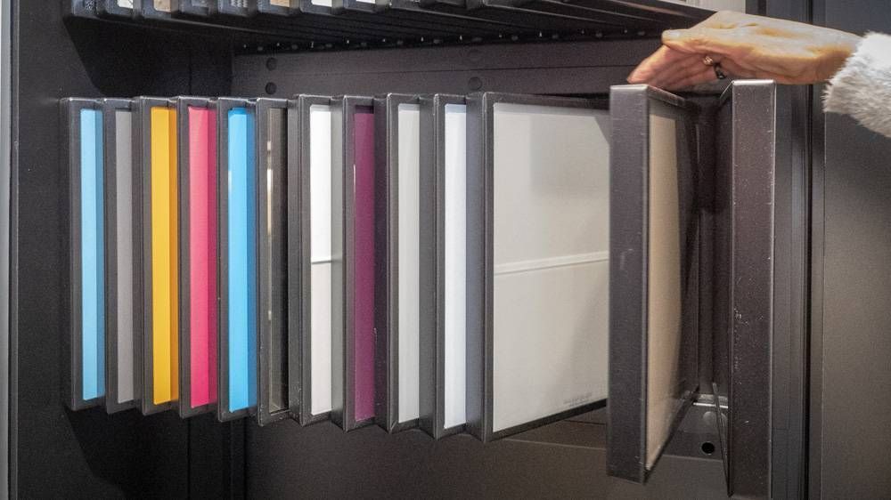 Rangée de chemises suspendues colorées et de classeurs sur une étagère, une main tenant la chemise tout en haut à droite