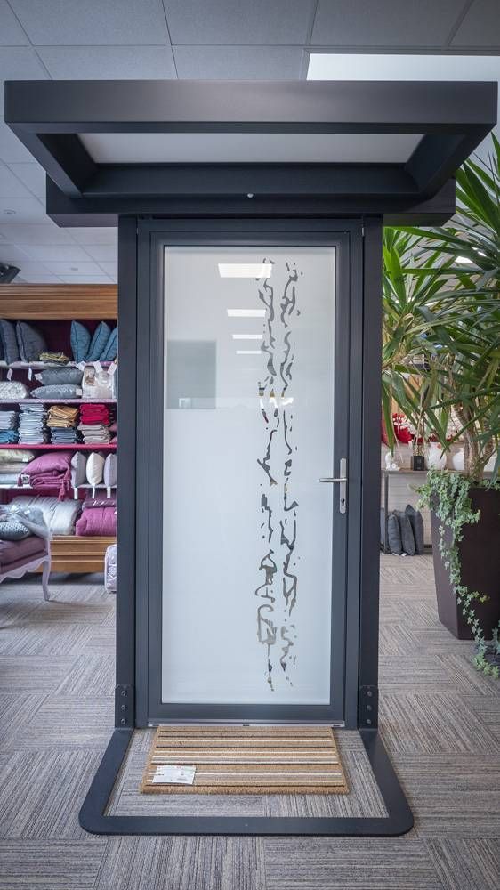Vitrine de porte vitrée moderne à cadre sombre, avec des panneaux dépolis et des bordures à motifs, à l’entrée d’un magasin