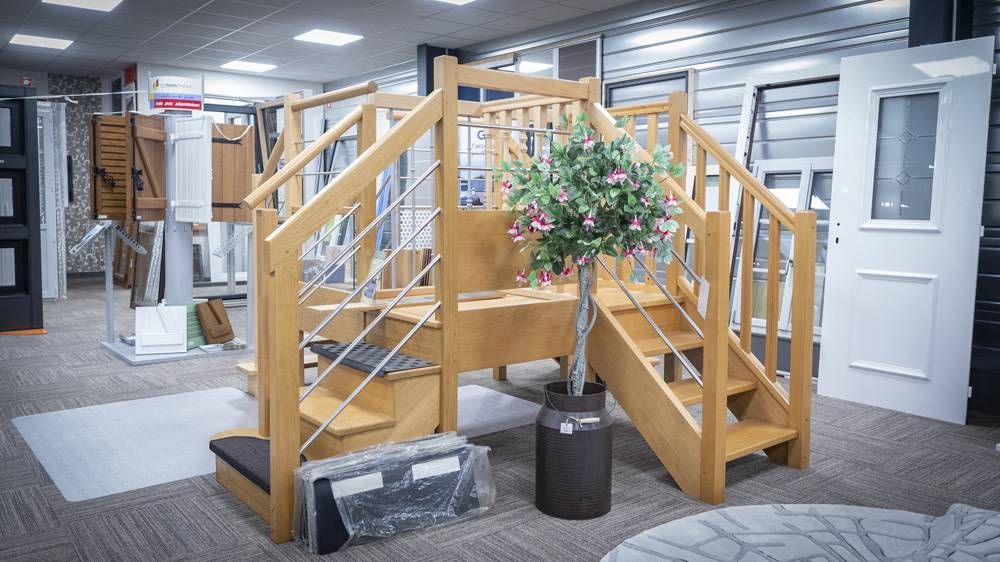 Escalier d’intérieur en bois avec rampes, une plante fleurie en pot et du mobilier de bureau en arrière-plan