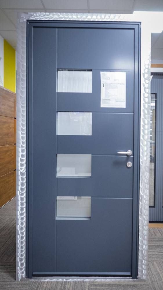 Porte grise avec quatre panneaux en verre dépoli et des avis affichés dans un couloir carrelé