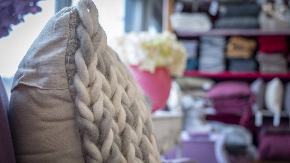 Gros plan d’un coussin tressé crème sur fond de salon légèrement flou.