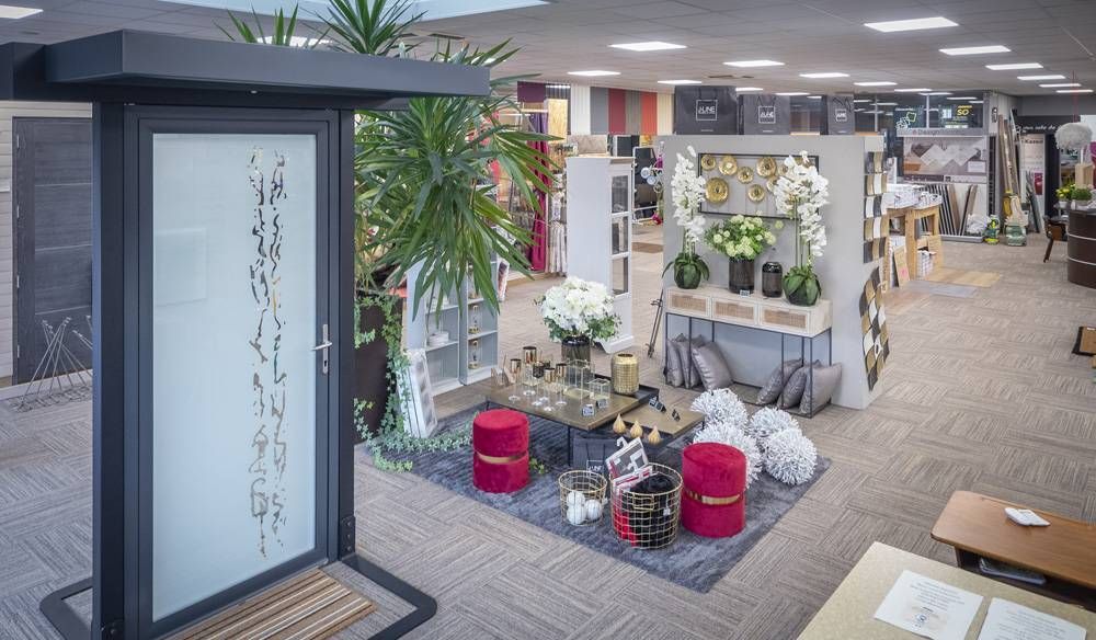 Salle d’exposition de bureaux avec un décor intérieur soigné, des plantes, des œuvres encadrées et des tapis dans un espace de travail moquetté