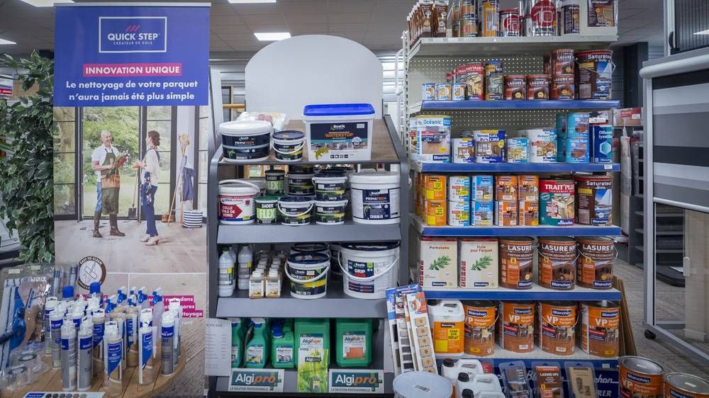 Rayon de magasin avec des étagères de boissons, de conserves et de snacks, ainsi qu’un petit présentoir et des paniers de courses.