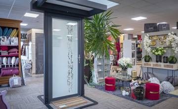 Showroom intérieur avec une présentation moderne de portes d’entrée, des plantes, des étagères et des objets décoratifs pour la maison