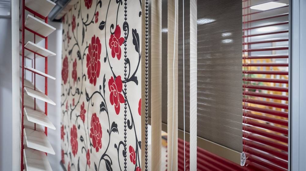 Intérieur de bureau moderne avec du papier peint fleuri, des cloisons vitrées et des stores blancs, à côté de volets rouges aux fenêtres