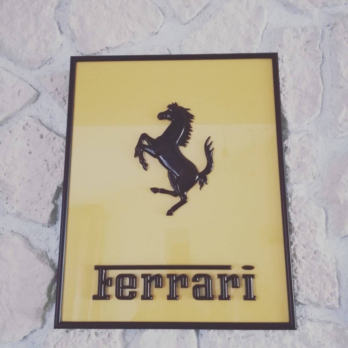 Logo Ferrari avec un cheval cabré noir sur une plaque jaune, devant un mur de pierre