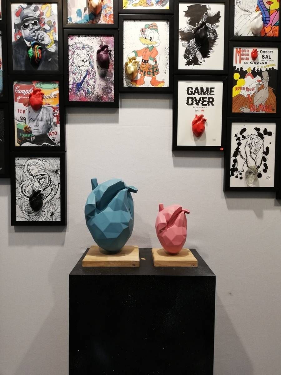 Mur de galerie avec des œuvres encadrées et deux sculptures géométriques sur un socle noir
