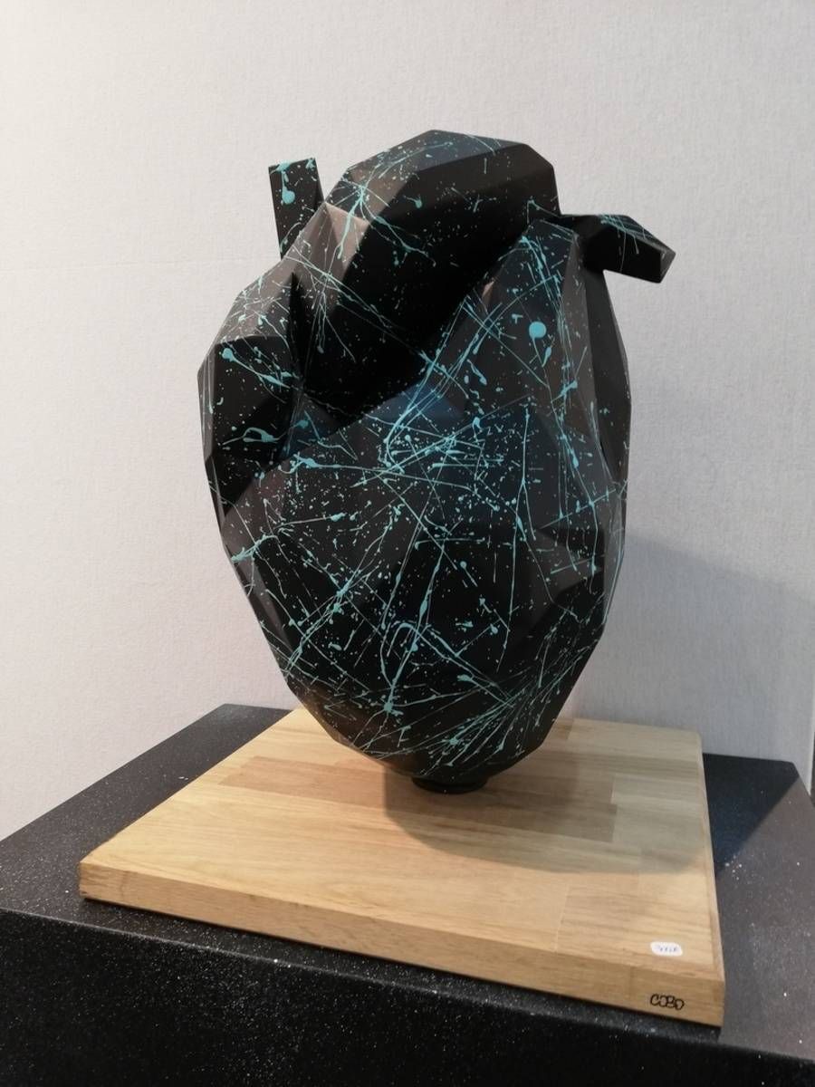 Sculpture noire abstraite avec des stries turquoise sur un socle en bois, devant un mur clair