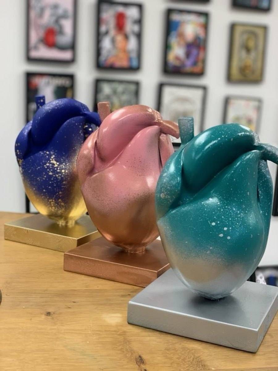 Trois sculptures abstraites d’oiseaux aux couleurs vives — bleue, rose et turquoise — exposées sur des socles en bois et en argent.