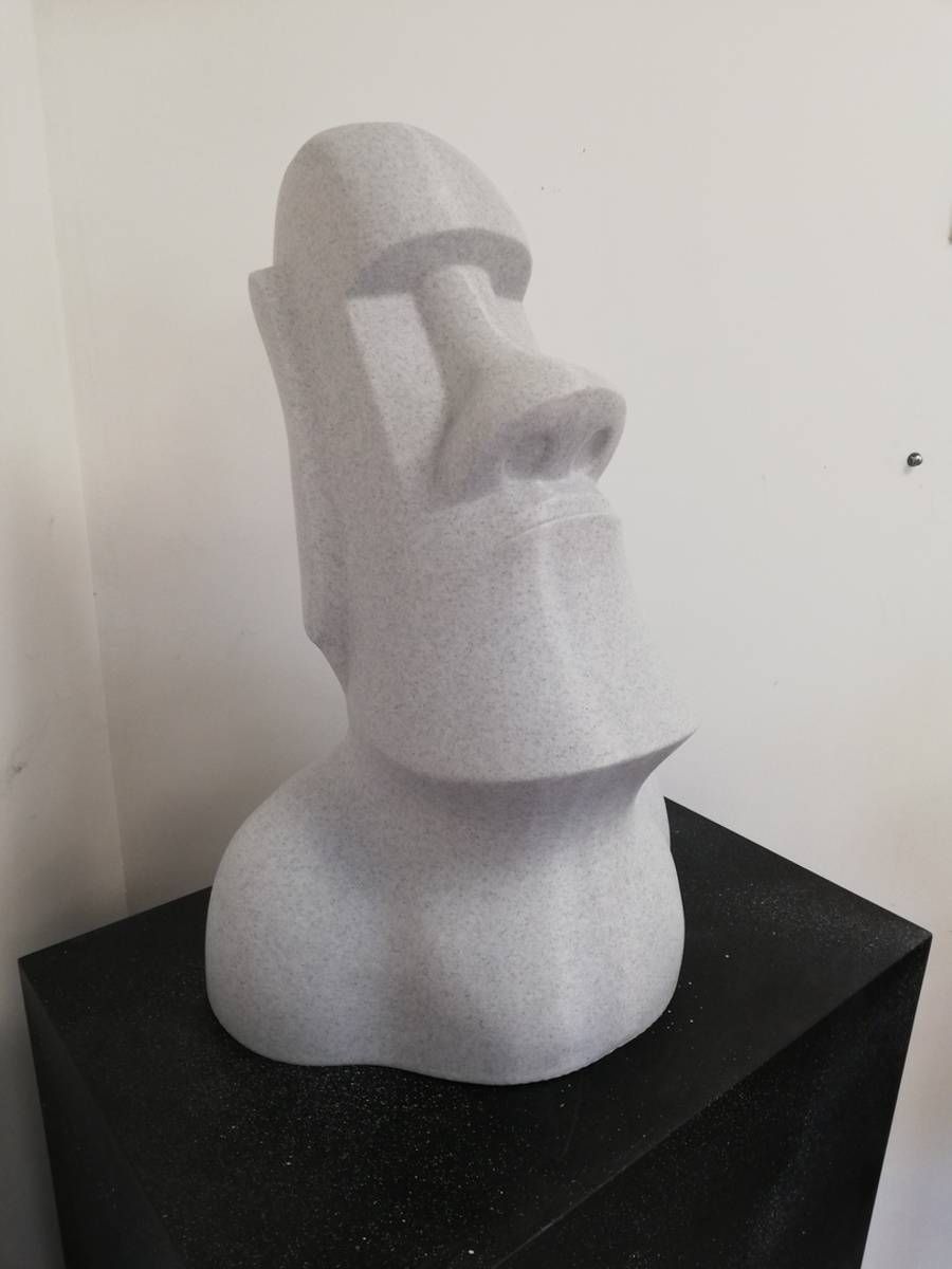 Buste abstrait blanc de style moaï sur un socle noir, devant un mur uni