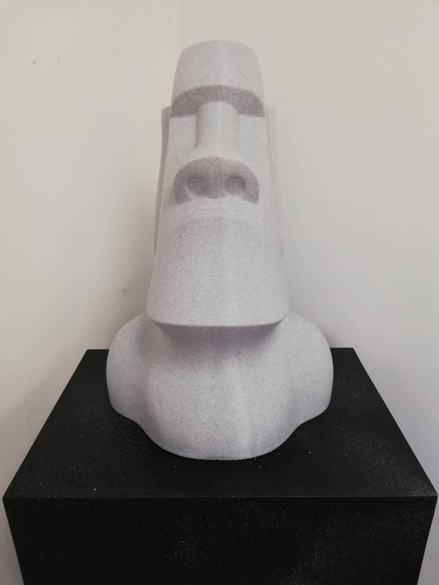 Sculpture blanche de style moai sur un piédestal noir, sur fond uni