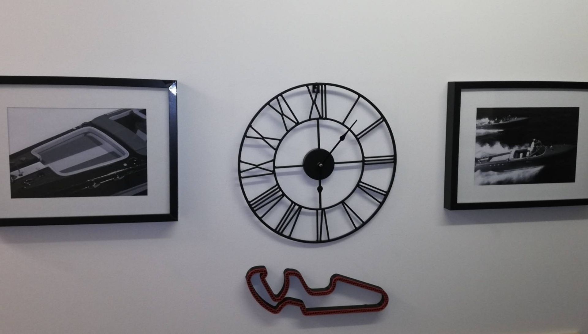 Mur avec deux photos encadrées de noir, une grande horloge en métal noir et une décoration murale rouge en forme de chaussure