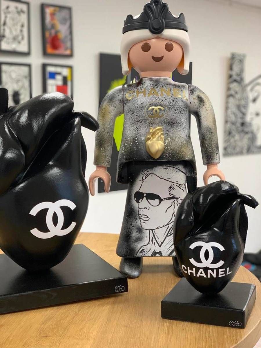 Figurine personnalisée avec une décoration et des logos Chanel en noir et blanc sur de petits présentoirs, contre un mur gris.