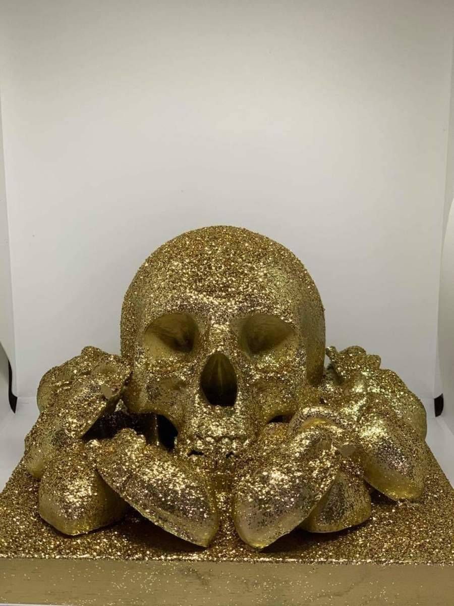 Sculpture de crâne doré à paillettes avec un socle orné de tentacules, sur fond blanc