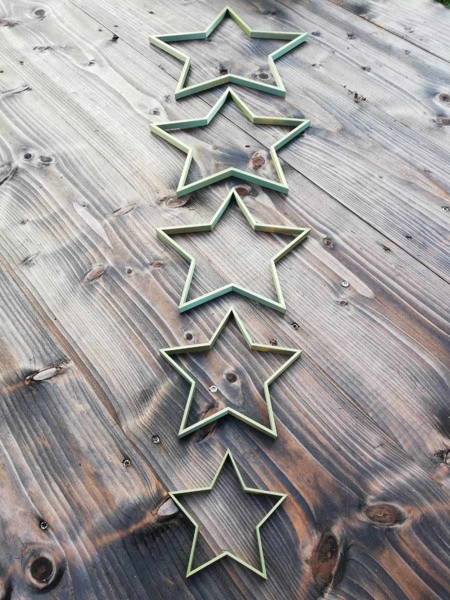 Cinq décorations en métal en forme d’étoile, bordées de vert, disposées en rangée verticale sur une surface en bois patinée