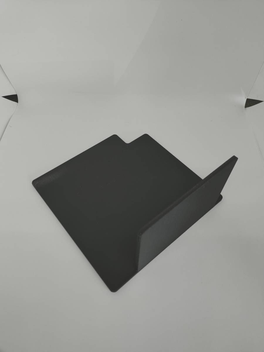 Support en papier noir plié posé sur une surface gris clair, avec de petits repères noirs aux coins.