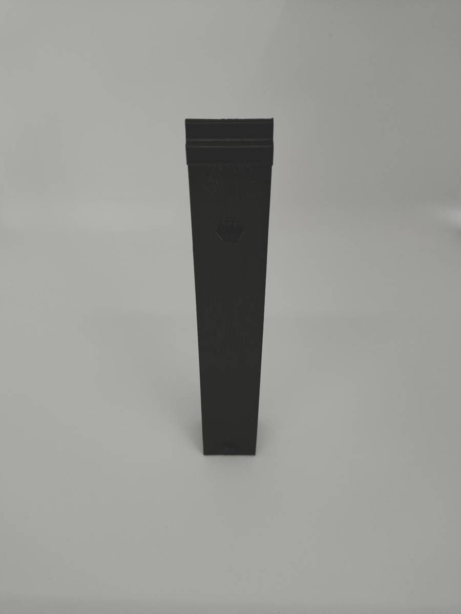 Objet rectangulaire noir à bords biseautés, posé à la verticale sur un fond gris clair