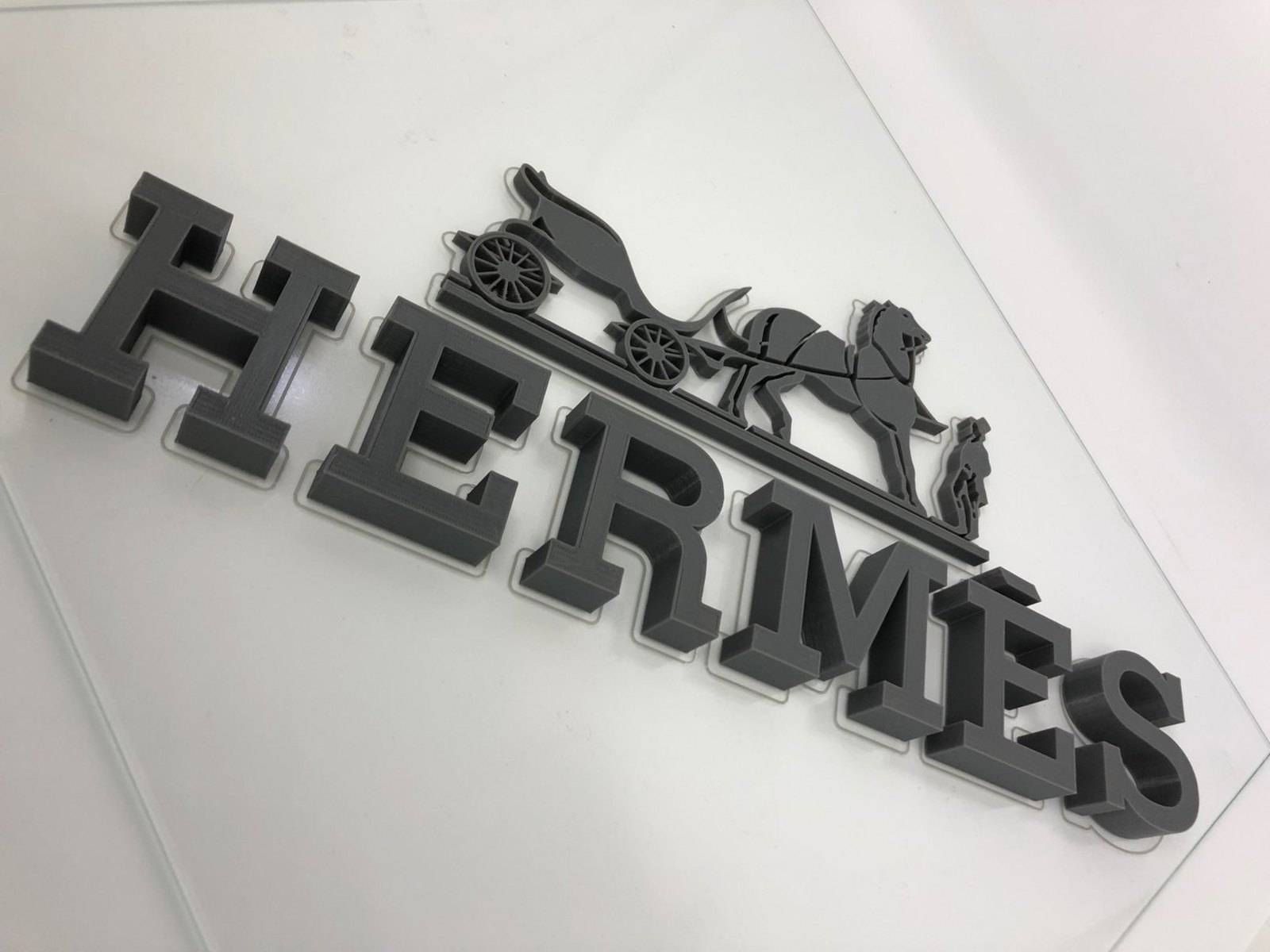 Enseigne HERMES noire représentant une silhouette de cheval et de cavalier sur un mur blanc