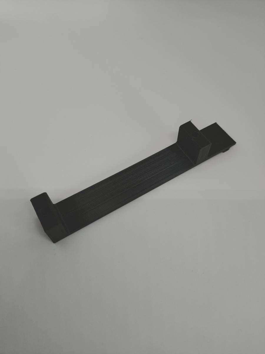 Support de téléphone en plastique noir avec des extrémités surélevées, posé sur une surface gris clair