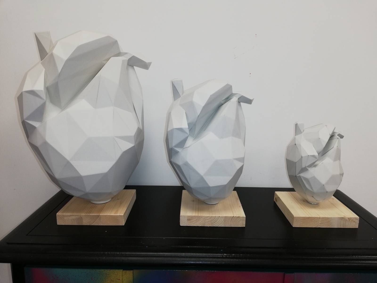 Trois sculptures de têtes d’animaux blanches à facettes, posées sur des socles en bois et disposées de la plus grande à la plus petite sur une étagère noire.