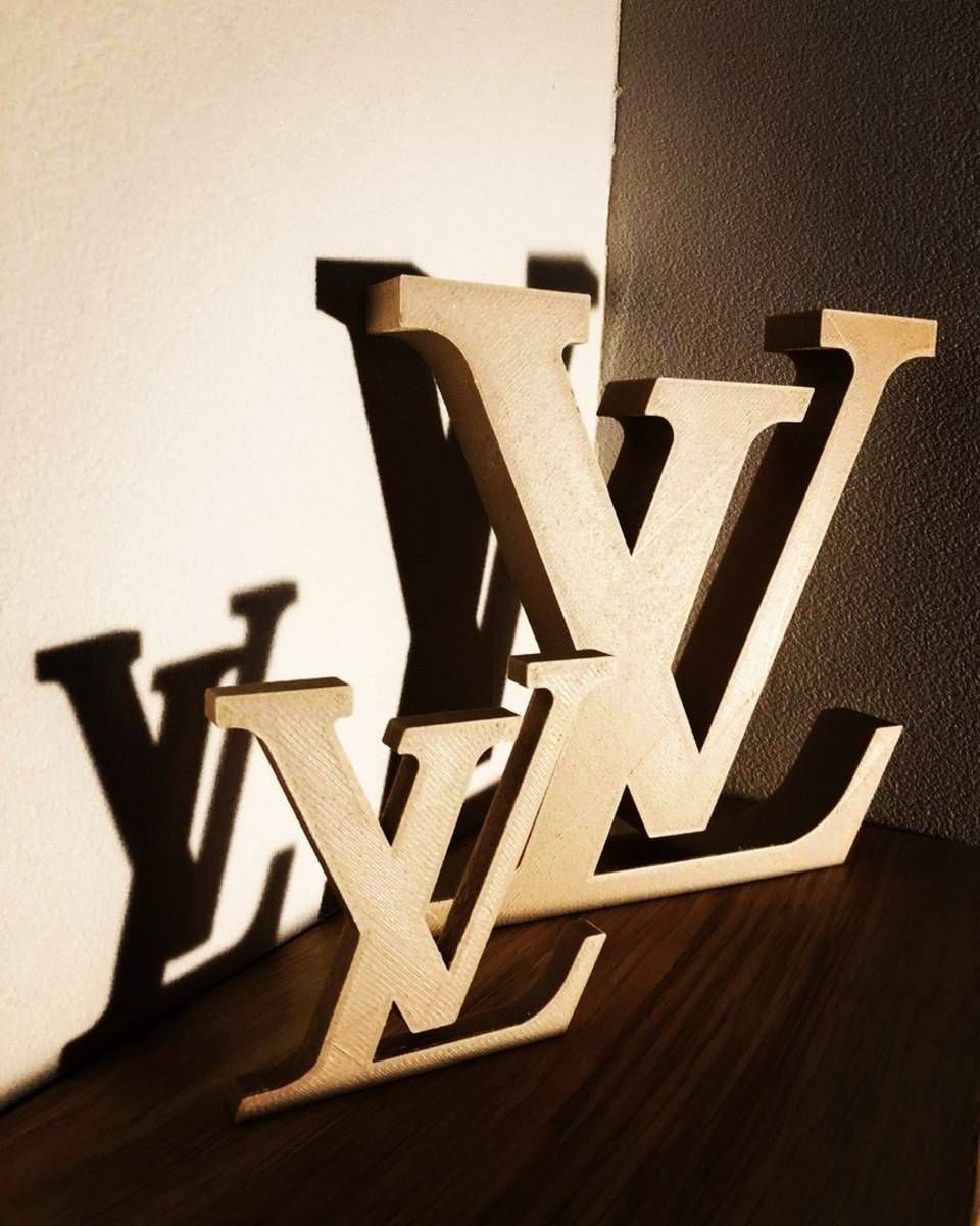 Trois lettres monogrammées Louis Vuitton superposées, en noir et beige, sur une surface en bois sombre