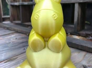 Figurine d’animal jaune avec des oreilles et des pattes arrondies, assise sur une terrasse en bois.