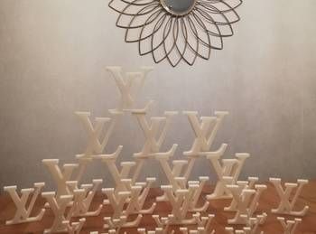 Composition décorative sur table représentant des monogrammes Louis Vuitton dorés empilés sous un ornement mural en métal
