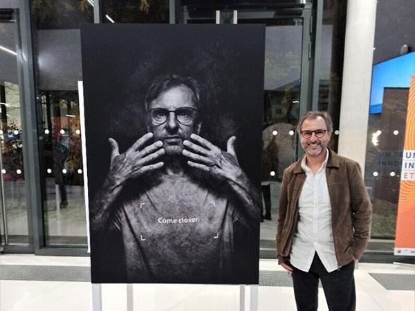 Un homme se tient à côté d’un grand portrait en noir et blanc dans une galerie aux murs vitrés.