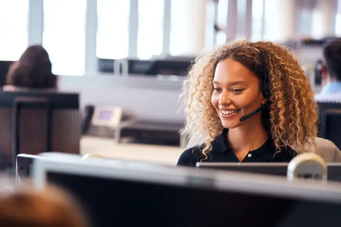 A woman is wearing a headset while sitting at a desk in front of a computer.