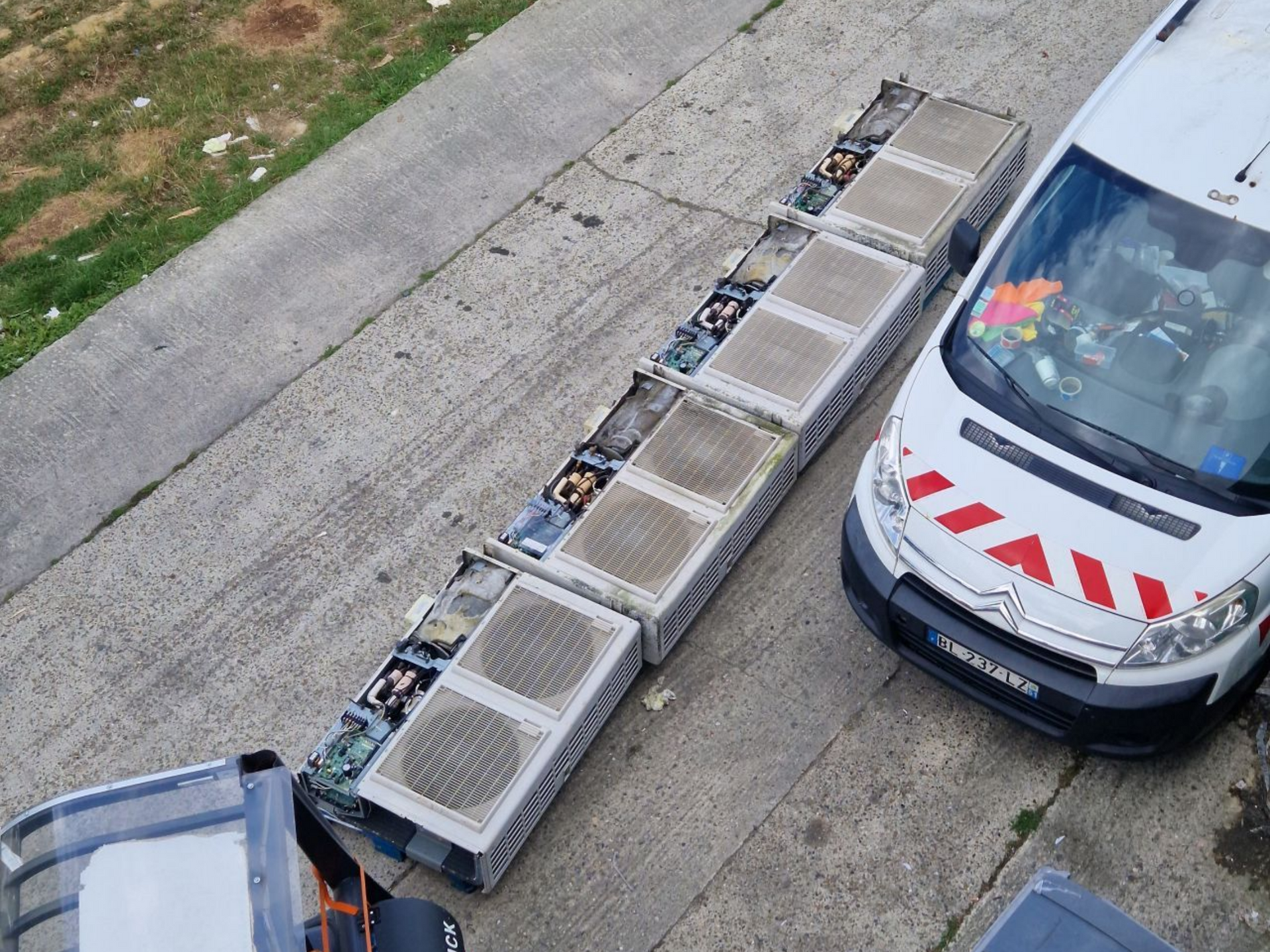 Plusieurs baies de serveurs rectangulaires sur le trottoir, à côté d'une camionnette blanche et d'un camion.