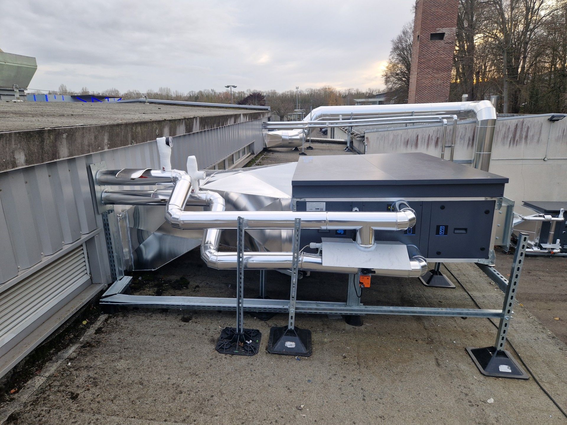 Équipement de climatisation sur un toit plat avec des tuyaux argentés, une unité métallique rectangulaire.