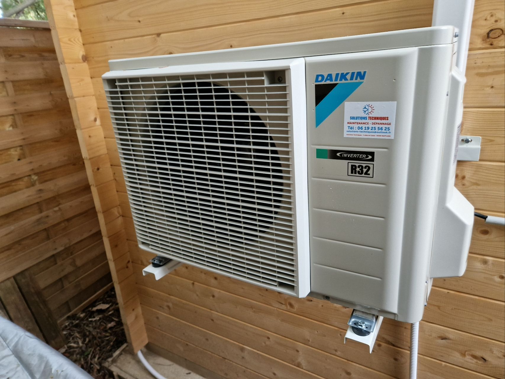 Unité de climatisation extérieure Daikin fixée sur un mur en bois.
