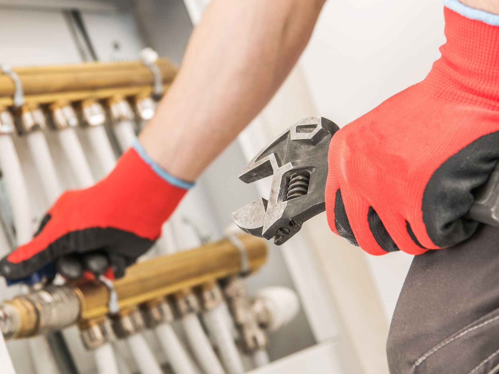 Personne portant des gants rouges utilisant une clé à molette sur des tuyaux.