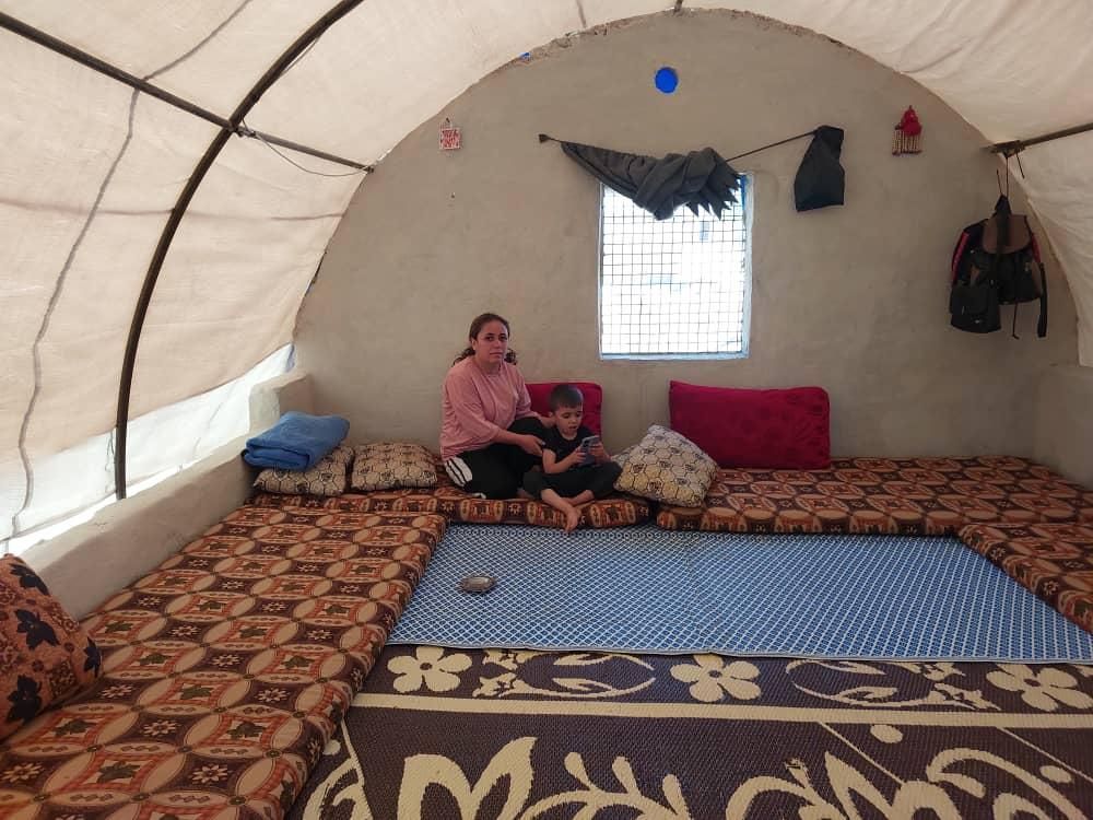 Eine Frau sitzt mit einem Kind in einem Zelt auf einer Couch