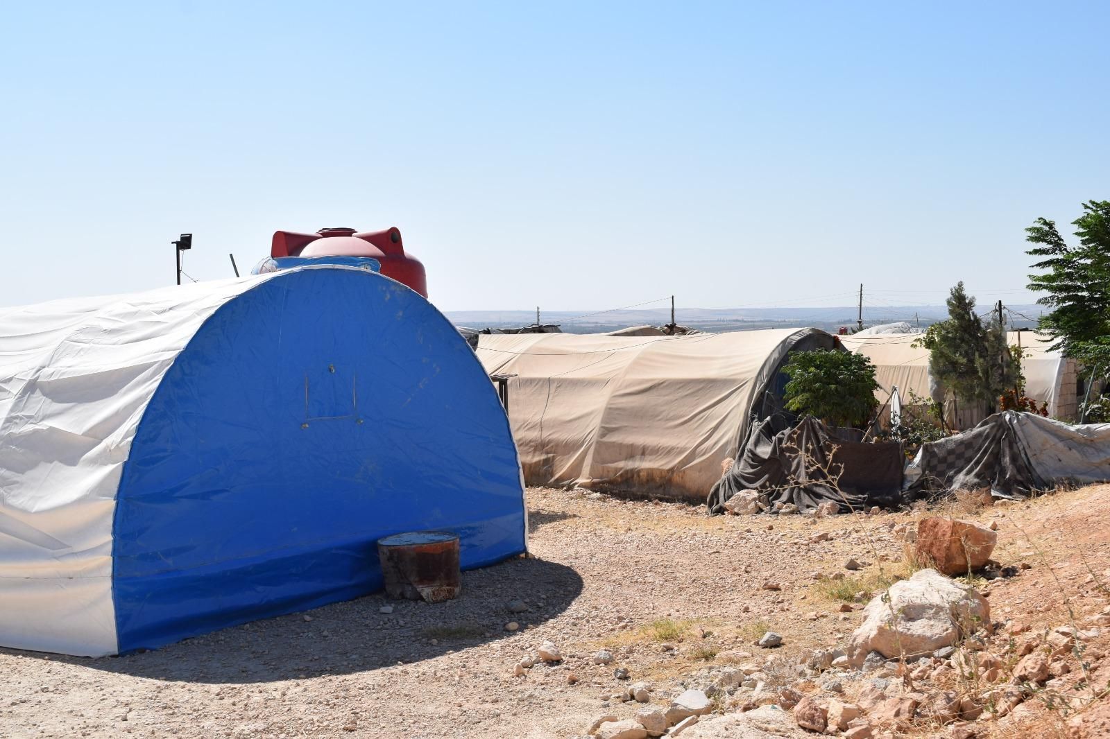A blue and white tent is sitting in the middle of a dirt field.